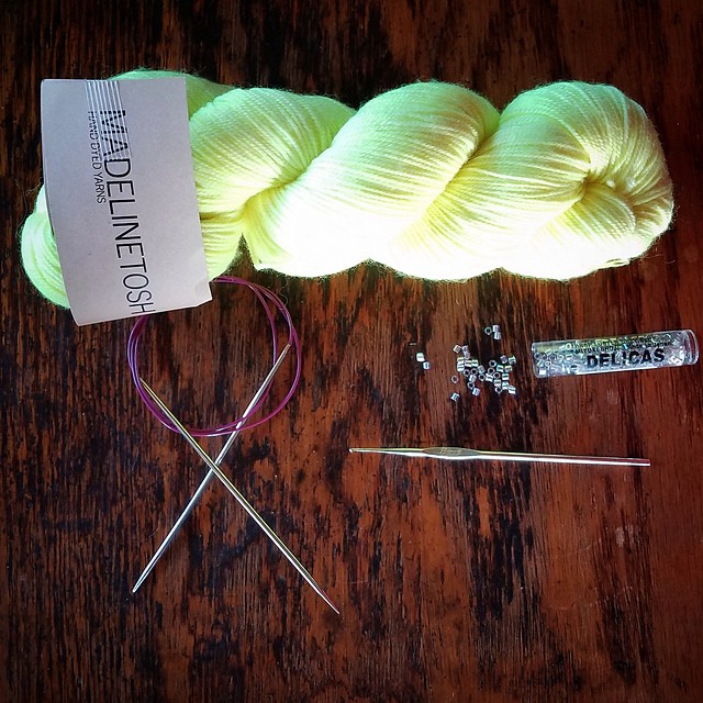 Neon yellow yarn, circular knitting needles, crochet hook, and beads